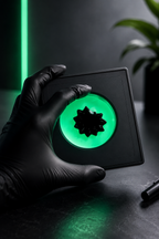 Hand wearing a black glove holding a glowing green object with a dark background